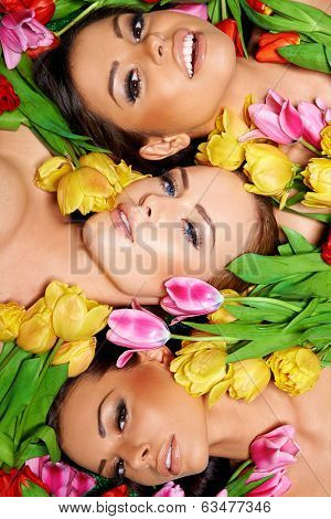 Three beautiful sensual women lying head to head surrounded by colorful spring tulips, overhead view as they look seductively up at the camera