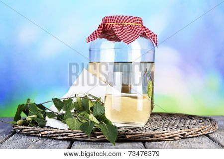 Flagon of birch juice on wicker round mat on wooden table on nature background