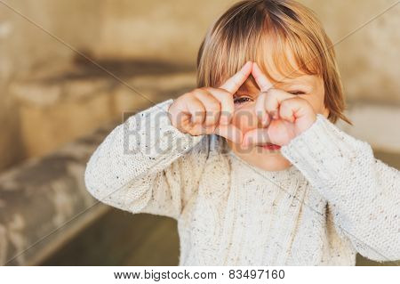 Outdoor portrait of a cute toddler boy pretending to take a picture with his hands