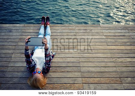 Young teen woman relaxing upon a wooden jetty while taking self portrait holding up tablet