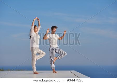 young couple practicing yoga at sunset in modern home terace with ocean and sunset in background