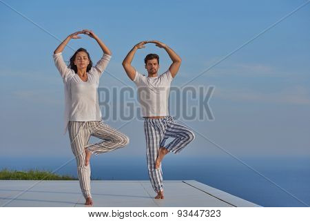 young couple practicing yoga at sunset in modern home terace with ocean and sunset in background