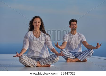 young couple practicing yoga at sunset in modern home terace with ocean and sunset in background