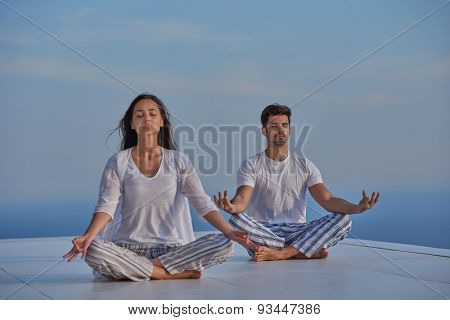 young couple practicing yoga at sunset in modern home terace with ocean and sunset in background