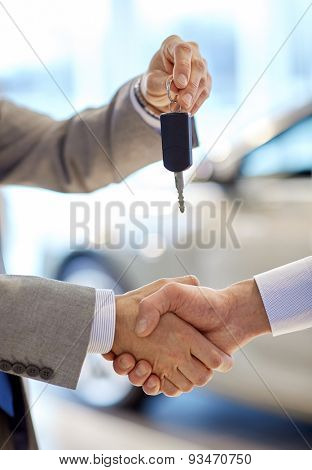 auto business, car sale, deal, gesture and people concept - close up of dealer giving key to new owner and shaking hands in auto show or salon