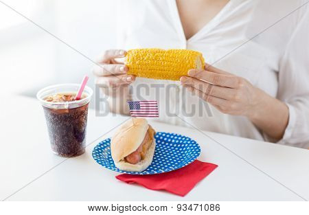 american independence day, celebration, patriotism and holidays concept - close up of woman hands holding corn with hot dog and coca cola drink in plastic cup on 4th july party