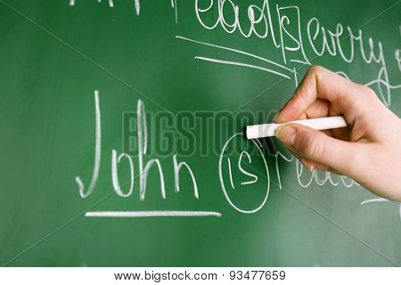 Teacher hand writing grammar sentences on blackboard background