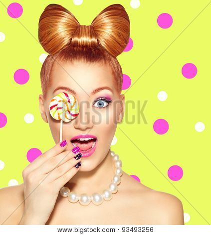 Beauty fashion model girl Eating colourful lollipop. Surprised Young funny woman with bow hairstyle, pink nail art and makeup over bright green with pink polka dots background