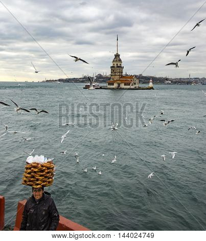 Istanbul Turkey - December 04 2013: Maiden Tower. A young salesman (Simit) bread vendor. European part of Istanbul in the background against the shore. Left Blue Mosque medium Hagia Sophia Topkapi palace dome seem right. The Maiden's Tower (Turkish: Kiz K