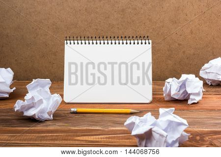 Searching an idea, motivation, result, dwaing scetches. White blank notepad book at office worplace crampled paper notes on wooden grunge background. Copy space for ad text