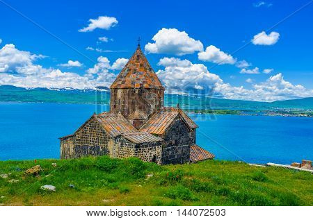The Surp Arakelots (Holy Apostles) Church of Sevanavank Monastery with the Sevan Lake and snowy mountains on the background Sevan Armenia.