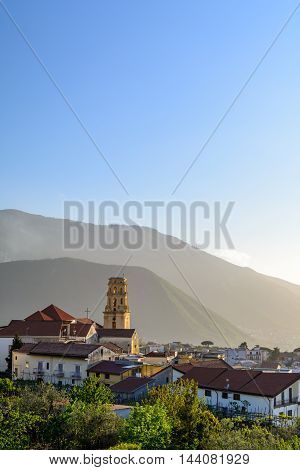 Spectacular view of coastal features in Italy. Vertical view with cliff side houses tower and church beautiful mountains in background.