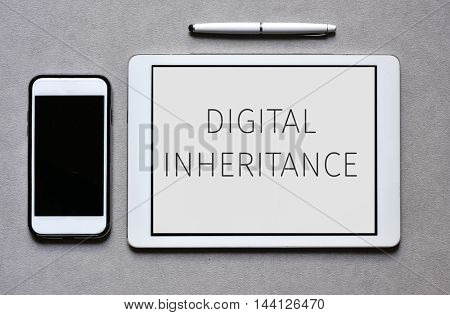 high-angle shot of a smartphone, a tablet computer with the text digital inheritance in its screen, and a digital pen on an elegant gray surface