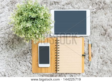 Closeup brown note book brown pen computer notebook tablet phone and artificial plant on gray fabric capet textured background in top view in work concept