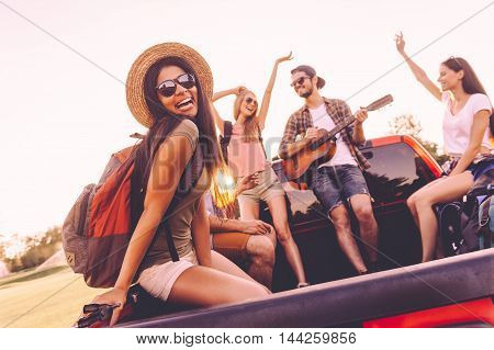 Enjoying road trip with best friends. Group of young cheerful people dancing and playing guitar while enjoying their road trip in pick-up truck together