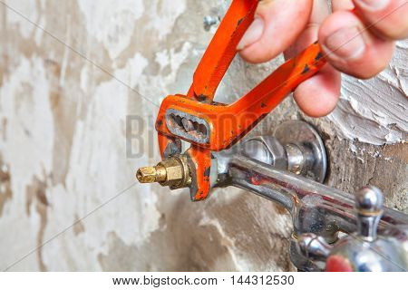 Plumber fixing water tap with leaking water users red plumber pliers.