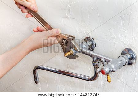 Plumber hands fixing water tap with spanner