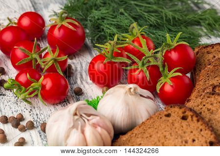 Still life on wooden background: tomatoes black bread garlic fennel bayberry pepper