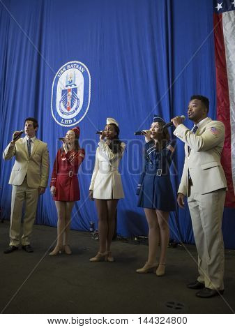 NEW YORK MAY 26 2016: USO Show Troupe pose/perform under the American Flag in the hangar bay of the amphibious assault ship USS Bataan (LDH 5) during the USO Build-A-Bike event during Fleet Week 2016.