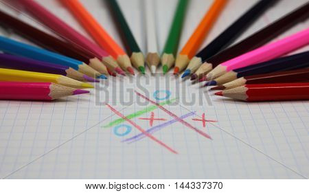 colored pencils and game a tic-tac-toe on a writing-book leaf
