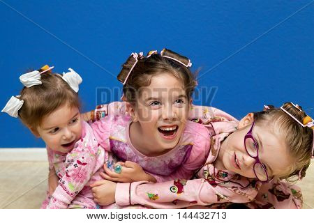 Three silly sisters a little hyper before bedtime hug in a pile on the floor while wearing curlers in their hair. They are ready for bed in their pajamas.