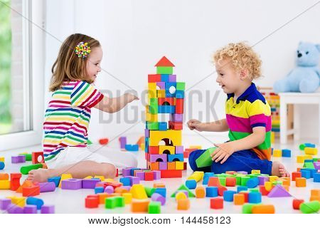 Happy preschool age children play with colorful plastic toy blocks. Creative kindergarten kids build a block tower. Educational toys for toddler or baby. Siblings having fun playing together.
