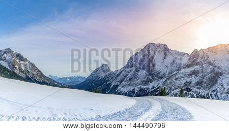 Alpine panorama with snowy road - Winter landscape with a road made by a snowmobile its traces through the layer of snow in the Austrian Alps mountains on a sunny day of December.