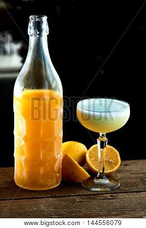 Alcoholic cocktail Limoncello sauer served in a glass wine glass and bottle on wooden table on black background