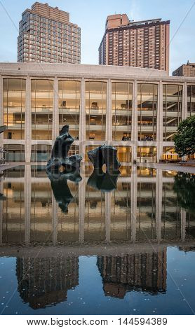 New York United States - June 20 2016: view of Henry Moore's bronze sculpture Reclining Figure (1965) in the pond basin at Lincoln Center with the reflaction. At same time the reflaction also includes the Every Fisher Hall in the background and highrise o