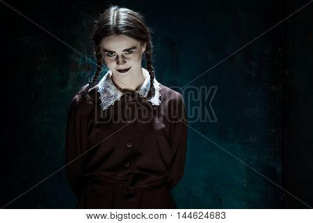 Portrait of a young smiling girl in school uniform as killer woman against school board . The image in the style of Halloween and Addams family