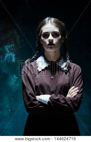 Portrait of a young girl in school uniform as killer woman against school board . The image in the style of Halloween and Addams family