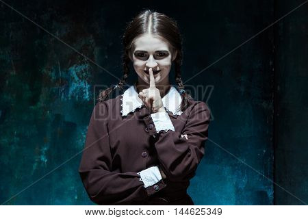 Portrait of a young smiling girl in school uniform as killer woman against school board . The image in the style of Halloween and Addams family