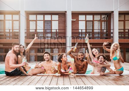 Croup of cheerful happy friends drinking beer at the pool outdoors