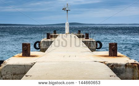 Old Pier With A Lighthouse Beacon And Calm Sea.