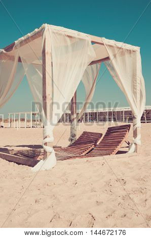 Gazebo on the beach with white curtains in the sand against the blue sky (vintage)