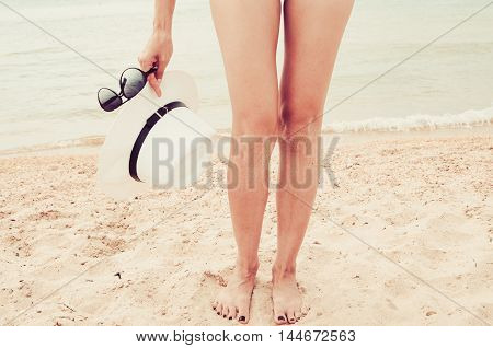 Women's feet in the sand. Beach accessories. Women's hat and sunglasses (vintage)