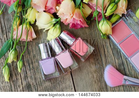 Nail polish, blush and brush on a wooden table on a background of beautiful flowers. Women's cosmetics