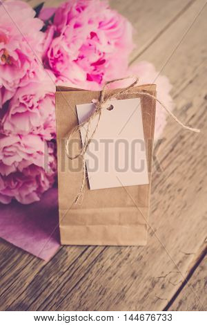 Kraft to pack gifts with a blank label for inscriptions or wishes on a wooden background next to a bouquet of flowers (Vintage)