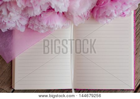 Open blank note pad decorated with pink peonies on a wooden background