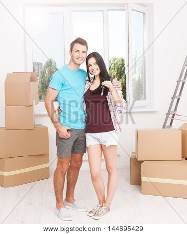Keys of their new house. Cheerful young couple holding keys and smiling while standing in their new house