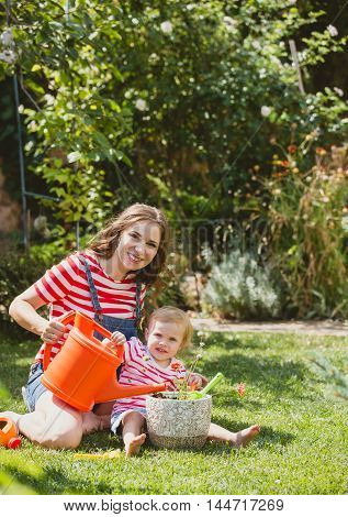 Pregnant woman with little daughter in the summer orchard cearing flower.