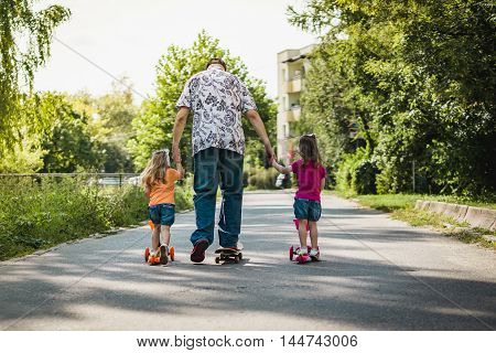 Dad with his daughters on a skateboard and scooter