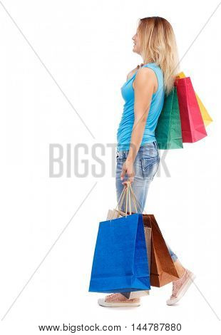 side view of going woman with shopping bags . beautiful girl in motion. Isolated over white background. The blonde in a blue t-shirt and jeans is going sideways to the camera with a paper shopping