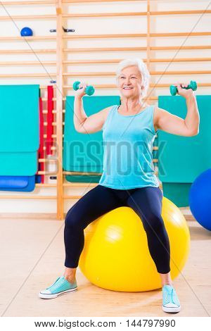 Senior woman doing fitness sport in gym with dumbbells
