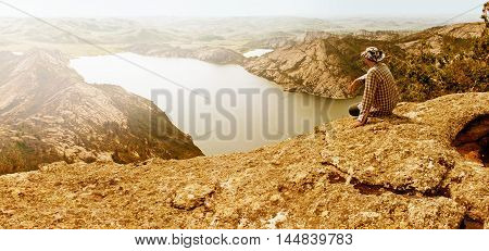 The man sitting on top of a mountain and looking over the lake and hills. Concept of leisure in weekand day