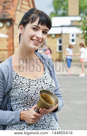 Portrait Of Teacher With Bell Supervising Break In School Playground