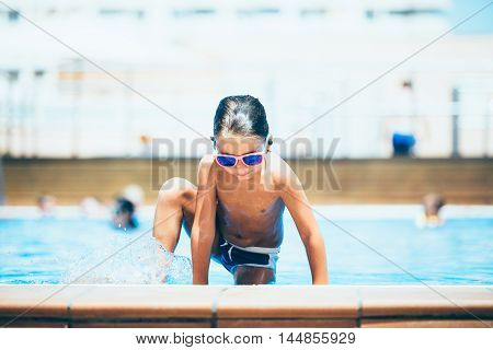 Portrait of wet-haired boy in sunglasses getting out of swimming pool in sunlight