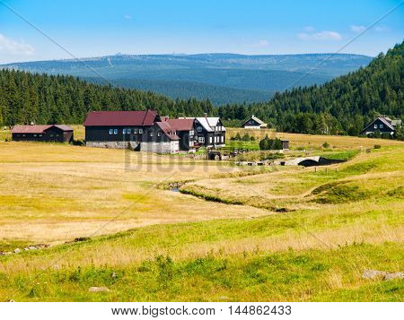 Large green meadows and rural mountain houses of Jizerka Village with Giant Mountains, or Krkonose, on the background, Jizera Mountains, Czech Republic.