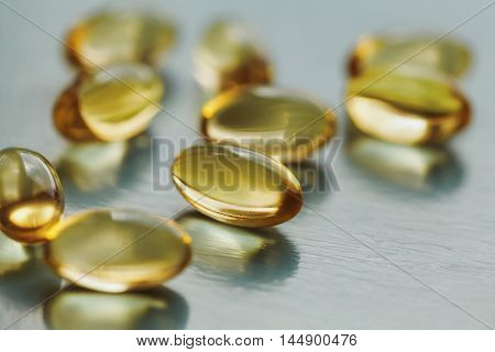 Yellow capsule with vitamin E tocopherol on blue surface, selective focus.