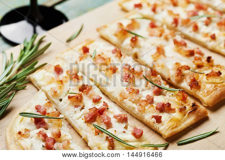 Tart Flambe or Flammkuchen on wooden cutting board decorated rosemary. Traditional Alsatian pie. Vintage style.